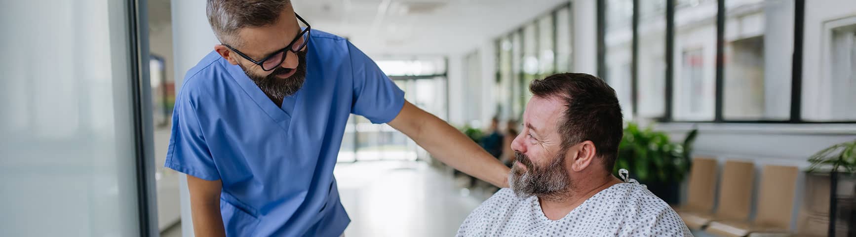 Healthcare provider speaking with a seated patient in a hospital hallway.