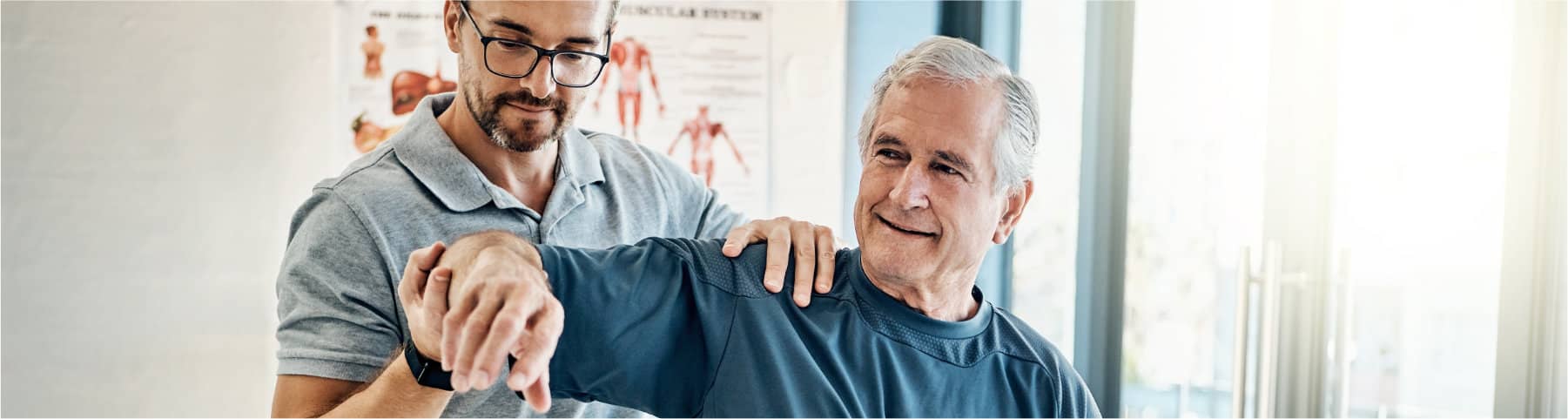 A therapist assists an older man with arm movement exercises in a rehabilitation clinic