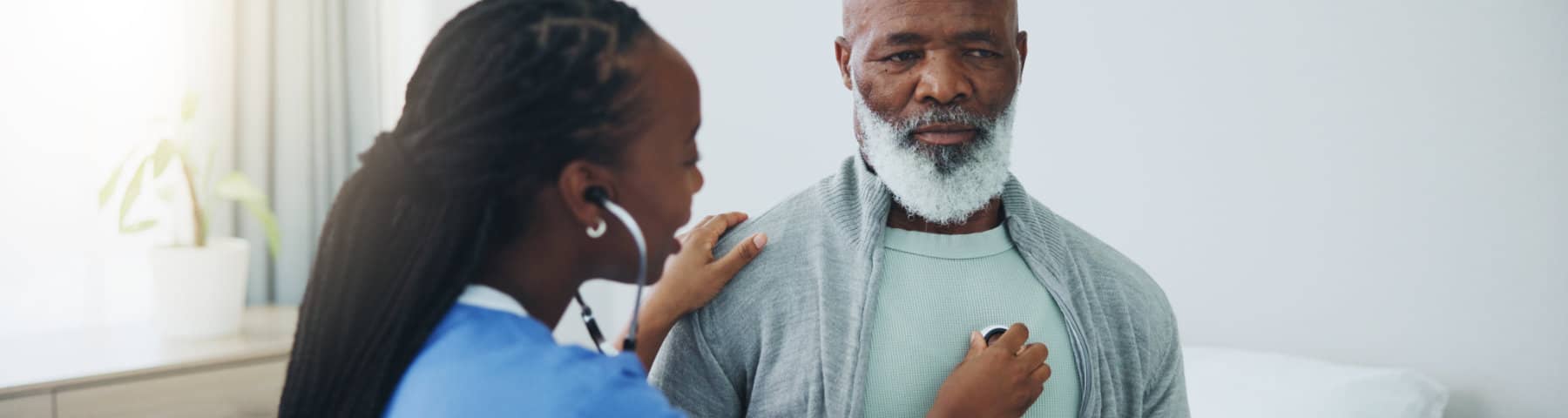 Healthcare provider listening to an older man’s chest with a stethoscope.