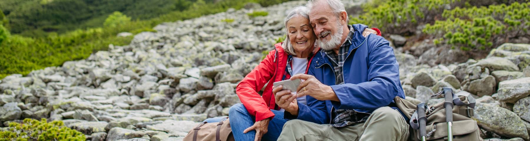 Older couple hiking and looking at a smartphone.