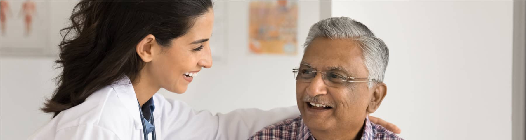 A doctor smiles and speaks reassuringly with an older male patient during a clinic visit