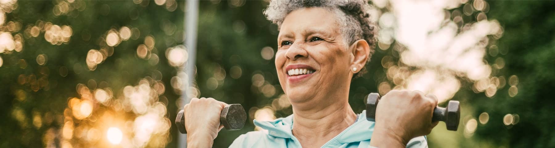 Older adult exercising outdoors while lifting light hand weights