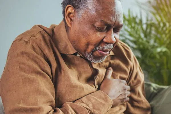 A man in discomfort holding his chest with his right arm.